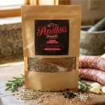 Parillo's Sweet Italian Sausage seasoning pack displayed on a wooden cutting board next to fresh raw sausage links, rosemary sprigs, garlic cloves, fennel seeds, black pepper, and coarse salt in a rustic kitchen setting
