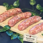 Four fresh Parillo's Retail Sweet Link sausages made with sweet pork, fennel and spices, displayed on a wooden cutting board with a product label tag, surrounded by green vine leaves on a dark background
