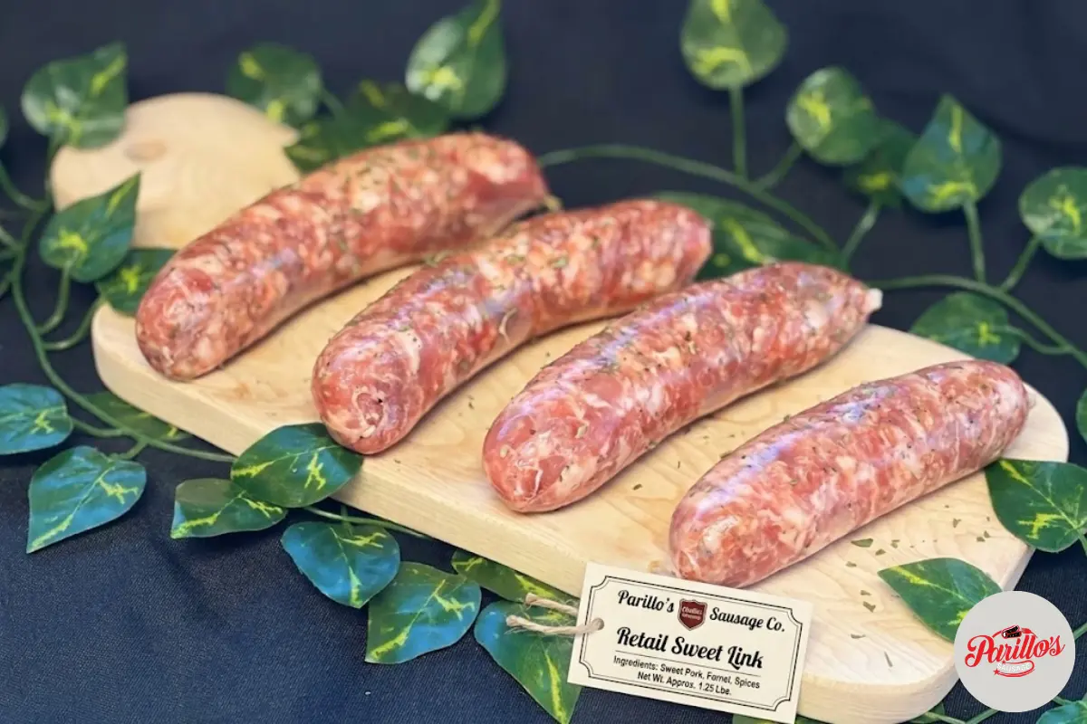 Four fresh Parillo's Retail Sweet Link sausages made with sweet pork, fennel and spices, displayed on a wooden cutting board with a product label tag, surrounded by green vine leaves on a dark background