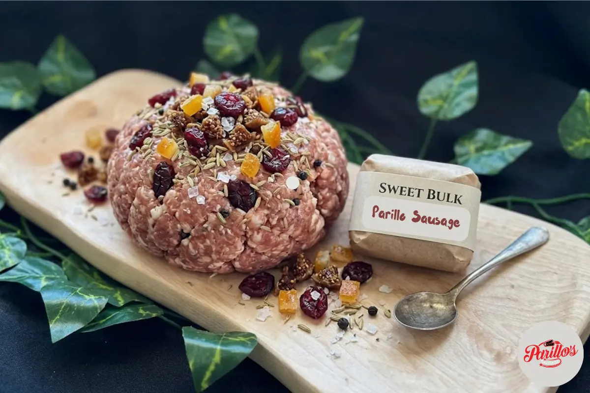 Parillo's Sweet Bulk ground sausage meat topped with dried cranberries, diced apricots, fennel seeds and coarse salt on a wooden cutting board with a Sweet Bulk Parillo Sausage label and vintage spoon, surrounded by green ivy leaves on a dark background